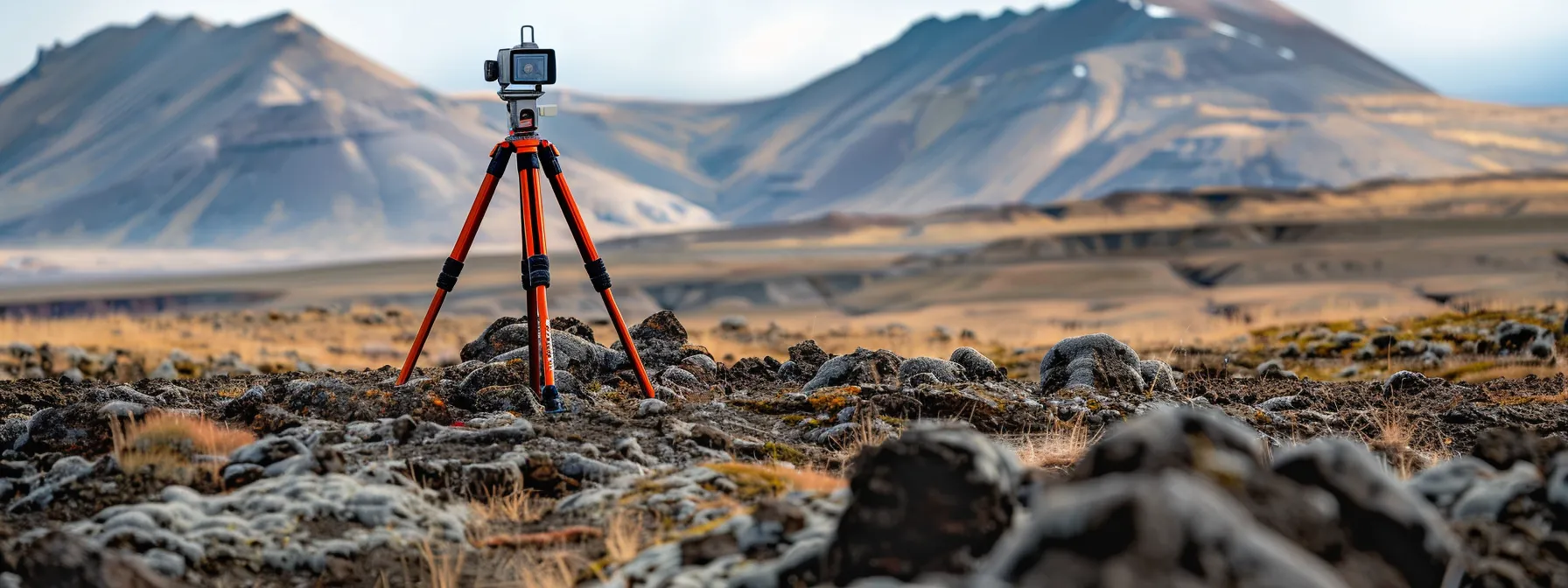 A sturdy tripod planted firmly on rugged terrain, with a total station securely mounted on top, ready for precise surveying operations.