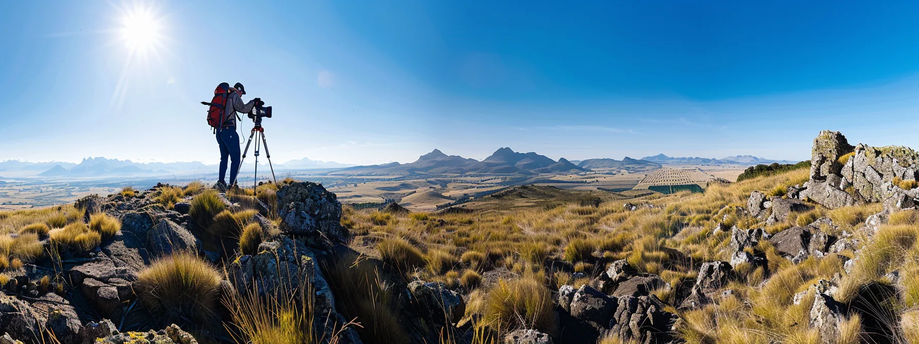 A surveyor adjusting the settings on a high-tech total station amidst a rugged, grassy landscape under a clear blue sky.